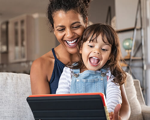 A woman viewing a tablet alongside a girl.